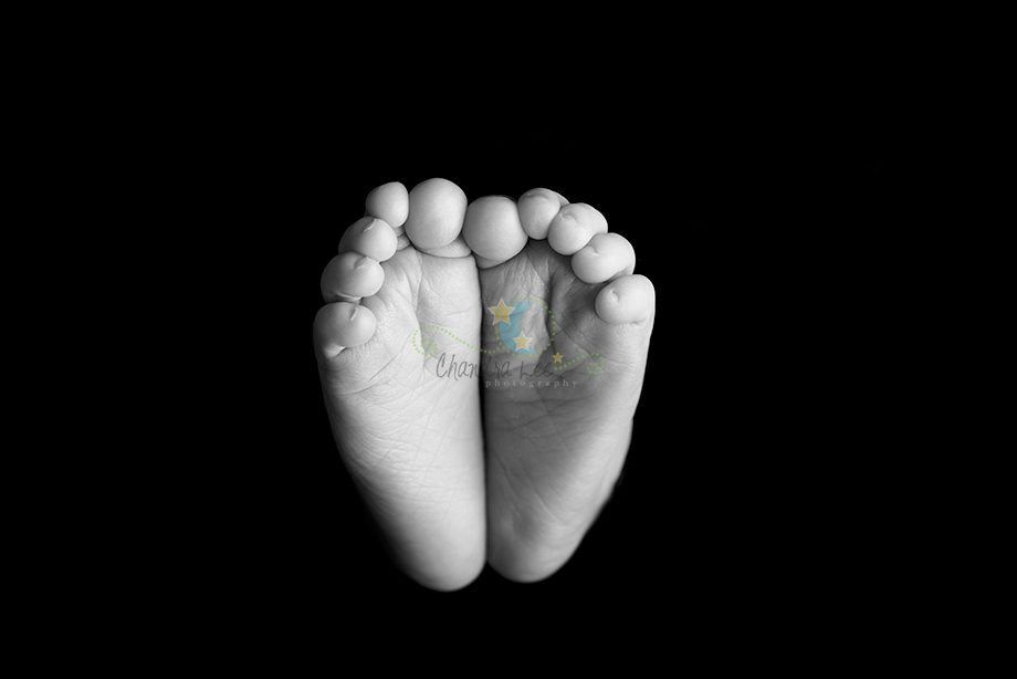 A close-up view of two feet positioned together, showing all toes. The feet are displayed against a black background in black and white.