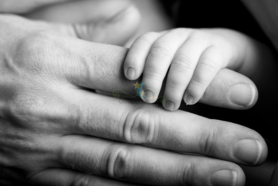 A close-up image of a child's hand gently resting on an adult's hand, both hands are shown in a black and white format. Details of the fingers and nails are visible.